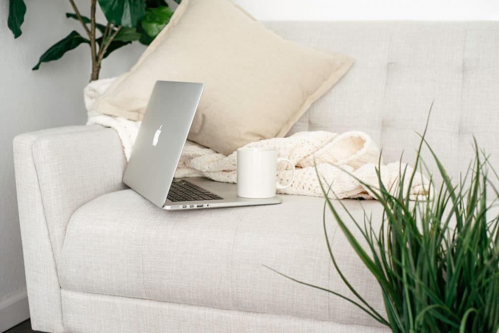 macbook on ivory couch with green plants and blanket