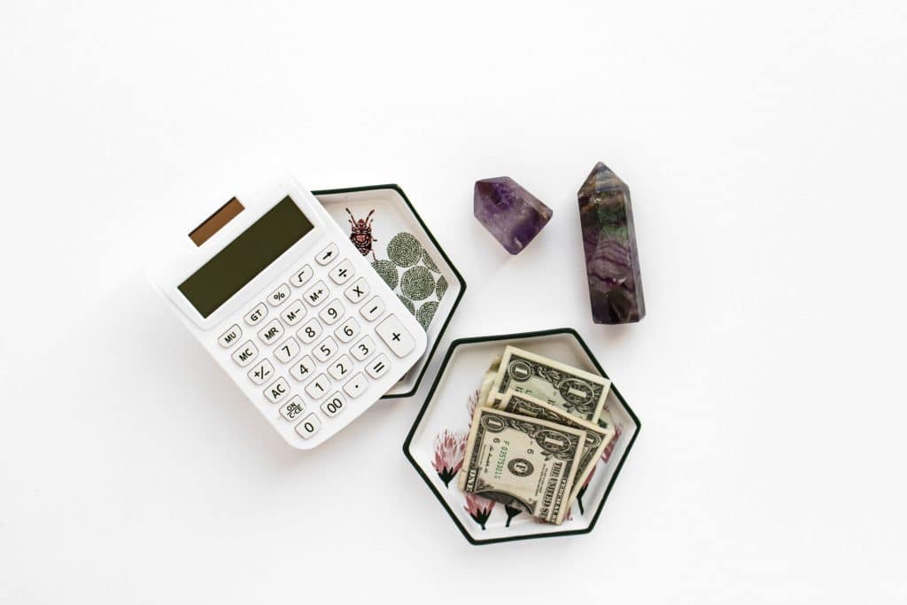 calculator with cash and healing crystals on white background