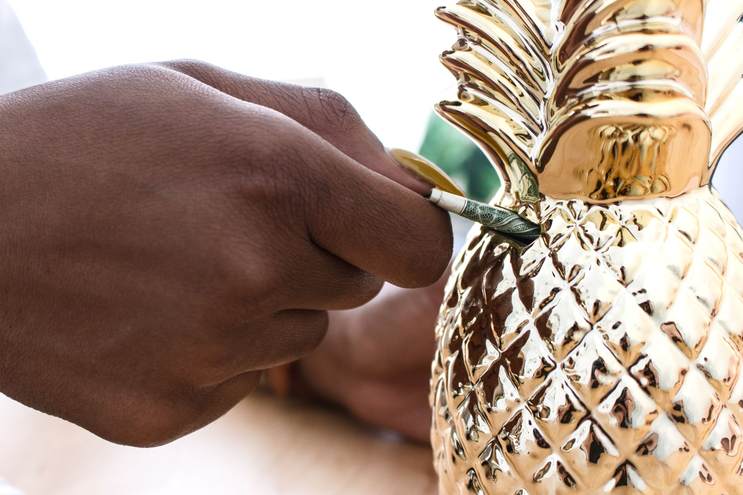 hand putting cash into pineapple piggy bank