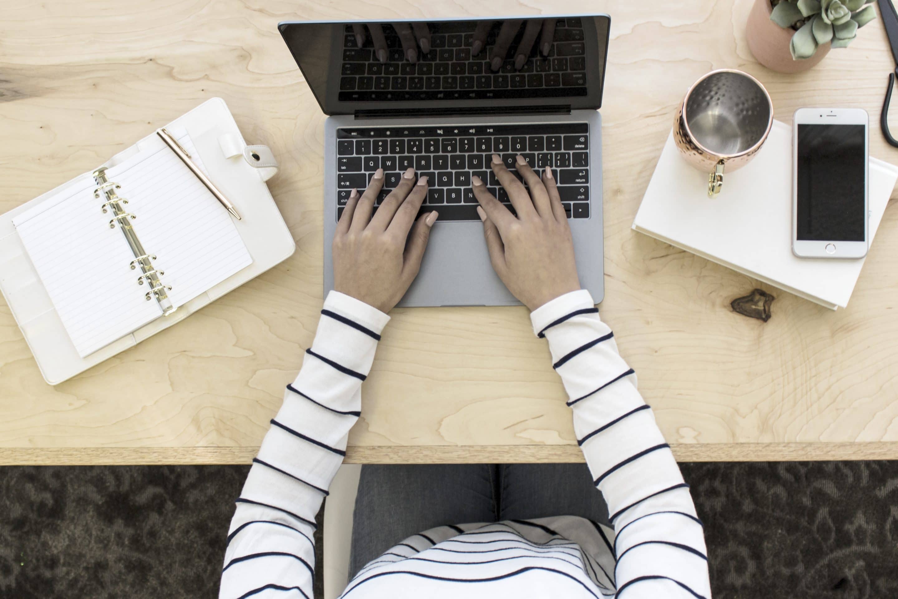 Woman typing on laptop with notebook
