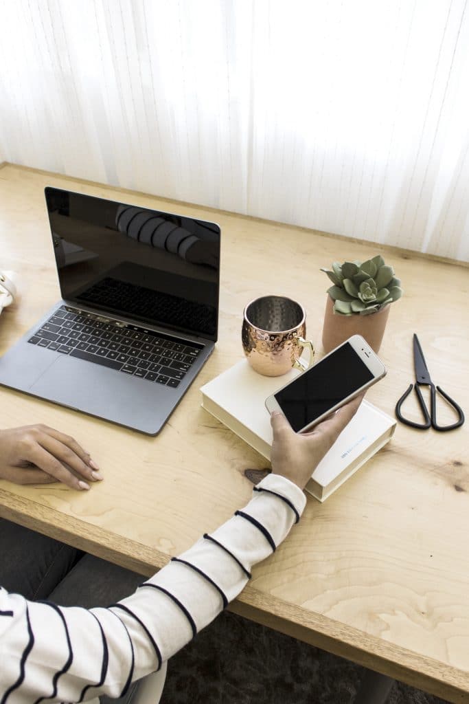 desk with computer and woman's hand holding cell phone