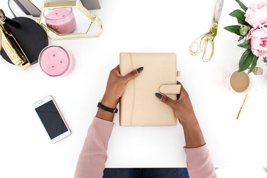 woman's hands holding tan planner with various office supplies.