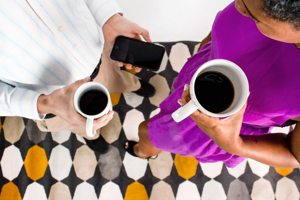 two office people holding coffee mugs and phones.