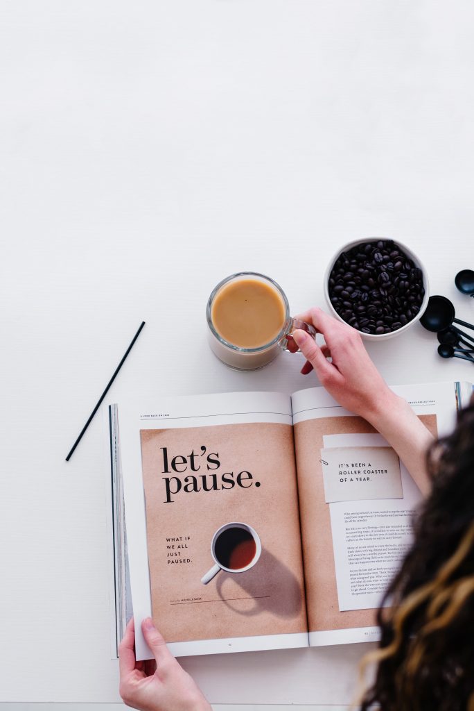 woman holding coffee cup and magazine on desk