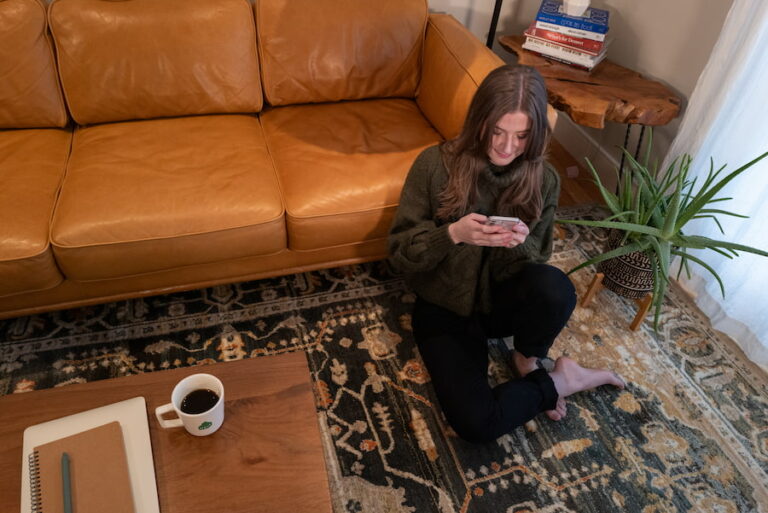 Chynna sitting on her living room floor in front of the couch looking down at her phone.