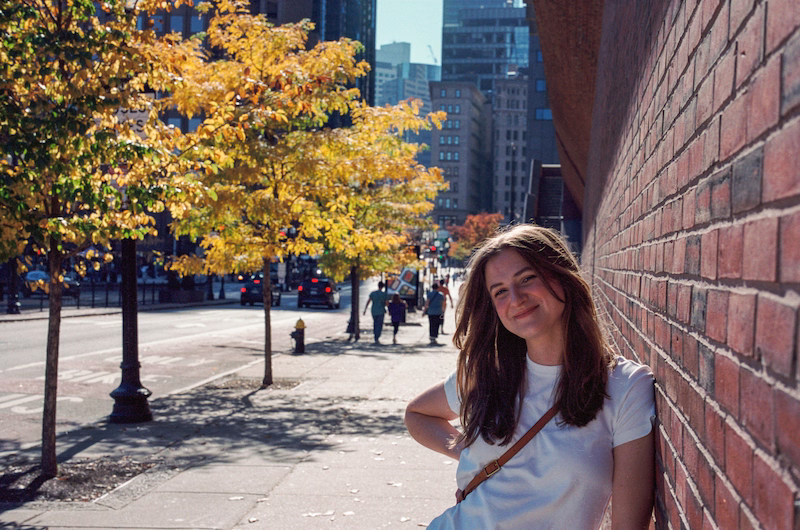 Chynna leaning on a brick wall. Wearing a white tshirt, hair down.