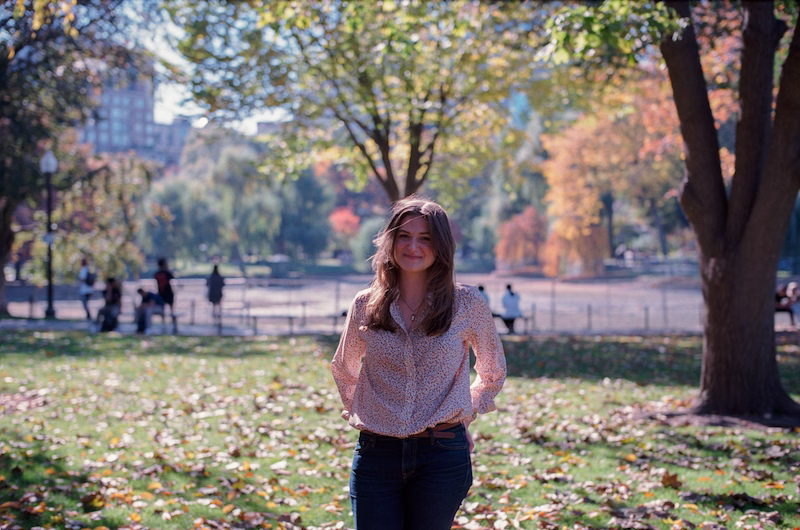 Chynna Benton standing in the middle of a park filled with trees and grass. She is wearing blue jeans, a red and white long sleeved shirt, and is wearing her hair down. Bith her hands are on her hips and she is smiling at the camera.