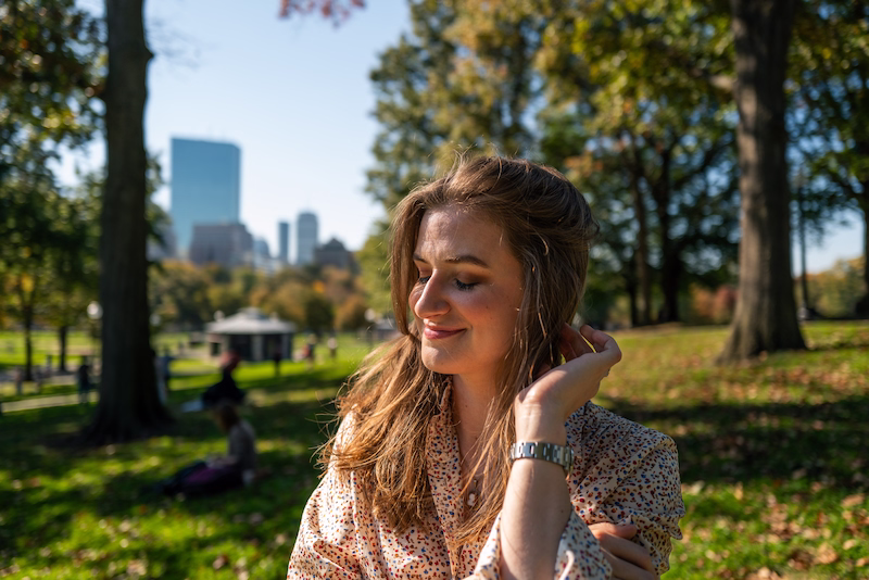chynna wearing a white and red shirt, pulling back her hair. Standing in a public park.