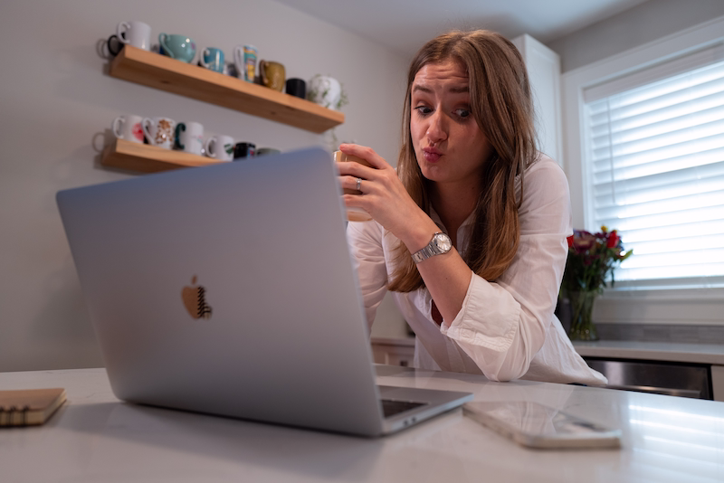 chynna at the kitchen island on her laptop. Holding a coffee cup and making a duck face.