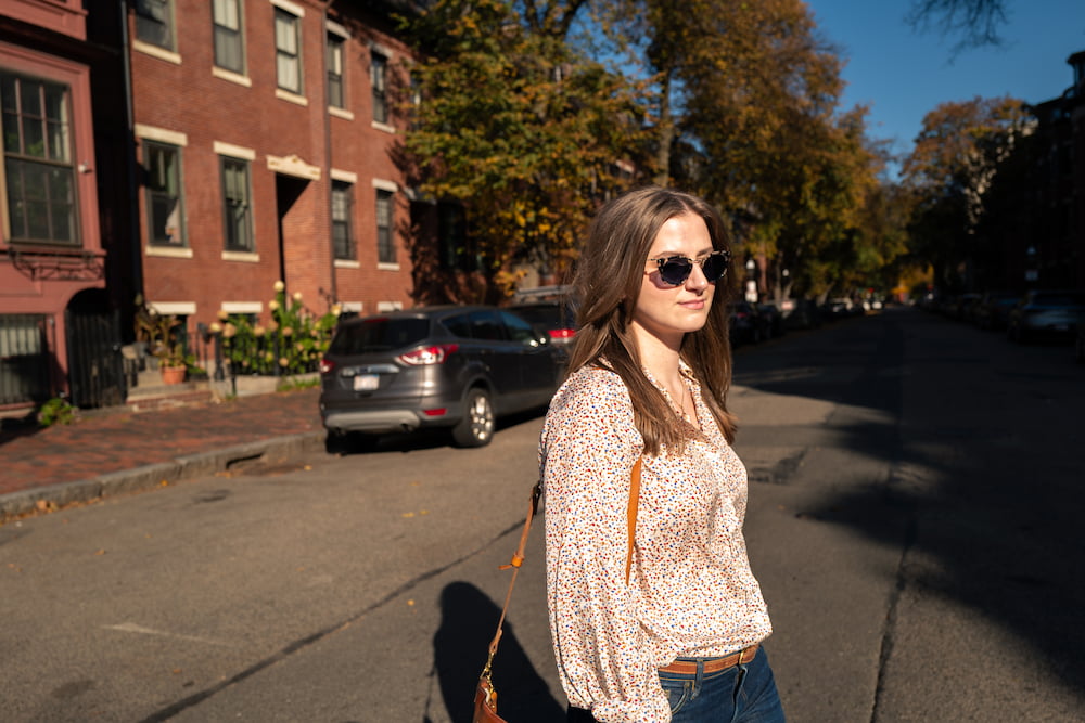 chynna walking outside down a brick home street wearing a beige shirt and wearing sunglasses