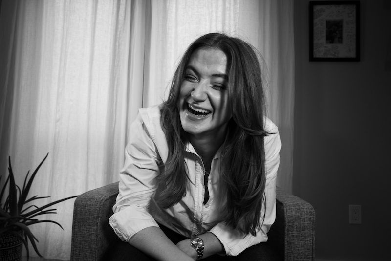 chynna laughing on a chair in front of a curtain window in black and white