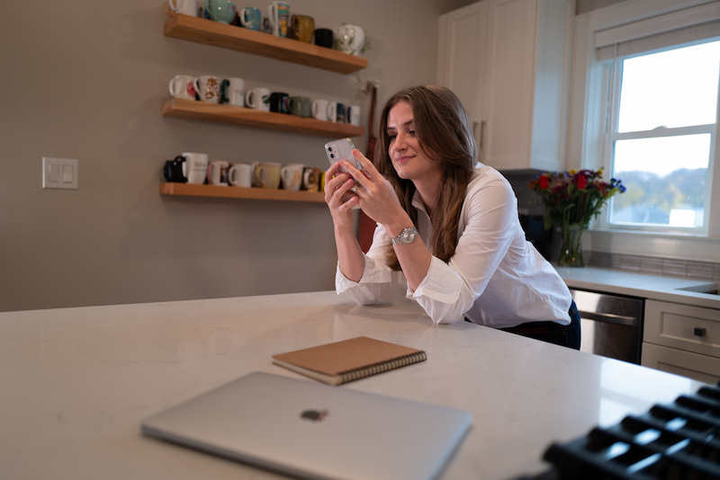 chynna on her cell phone and leaning on the kitchen island wearing a white button up
