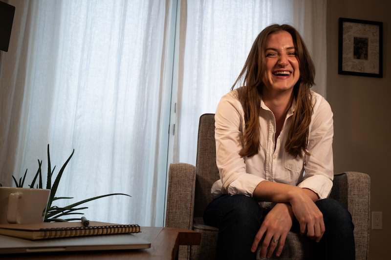 chynna benton sitting in her living room smiling in an armchair in front of a white curtain backdrop