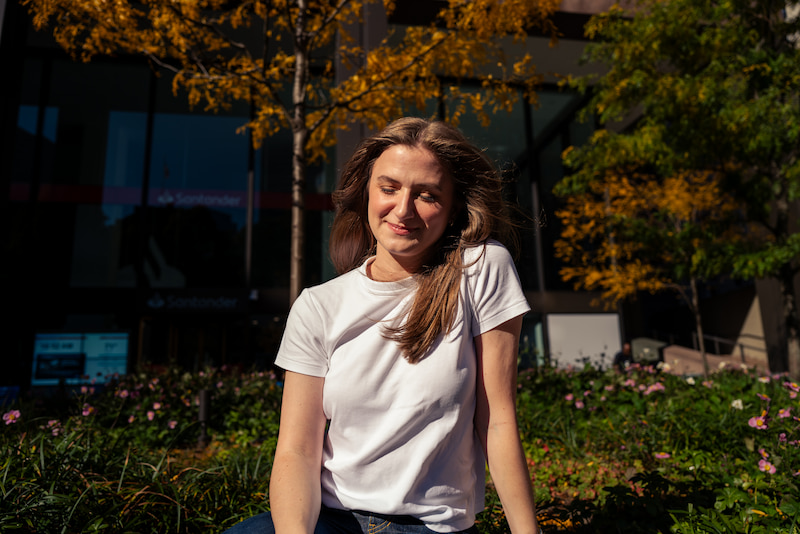Chynna Benton sitting outside in front of a garden in a white t-shirt and smiling while looking down