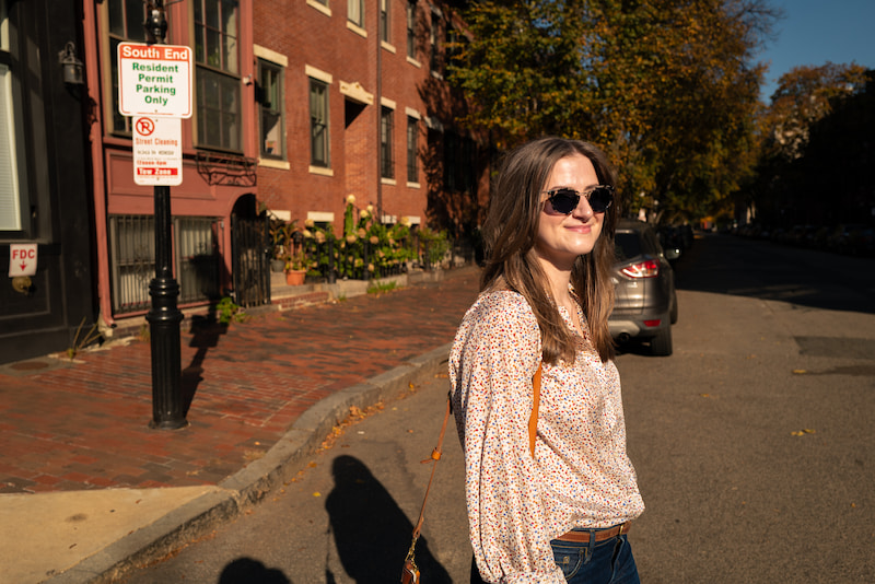 Chynna Benton walking through the South End of Boston wearing sunglasses and smiling to something in the distance
