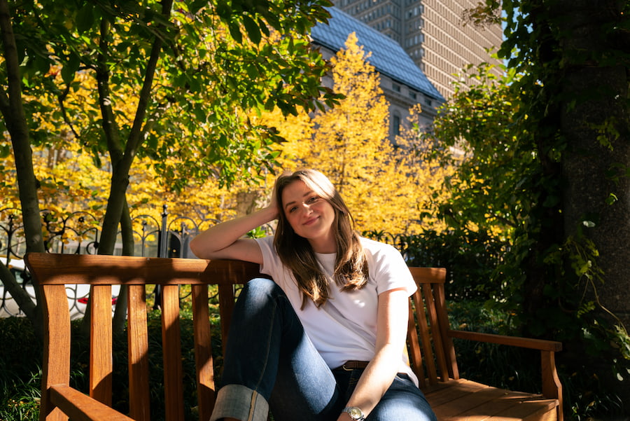 Chynna Benton sitting outside on a park bench in a white t-shirt and jeans, smiling at the camera in a calm way