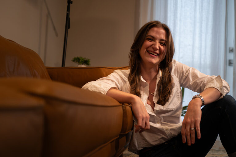 chynna sitting on the floor by her couch in a white button up laughing